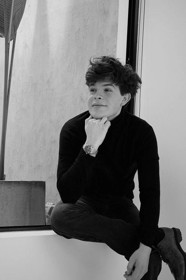 Juan F. Gutierrez sitting on a windowsill in a black turtleneck, in black and white.